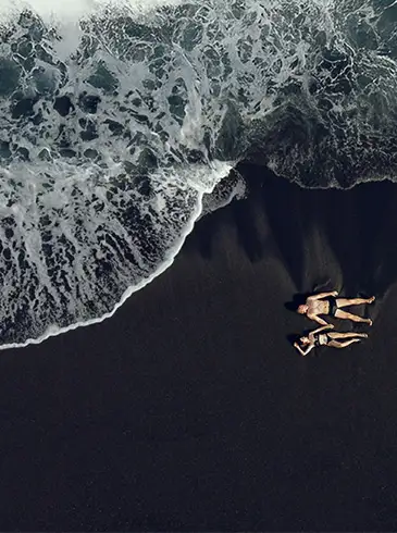 Eltern halten ihre Tochter an den Händen und laufen am Strand aus dem Meerwasser heraus. 
