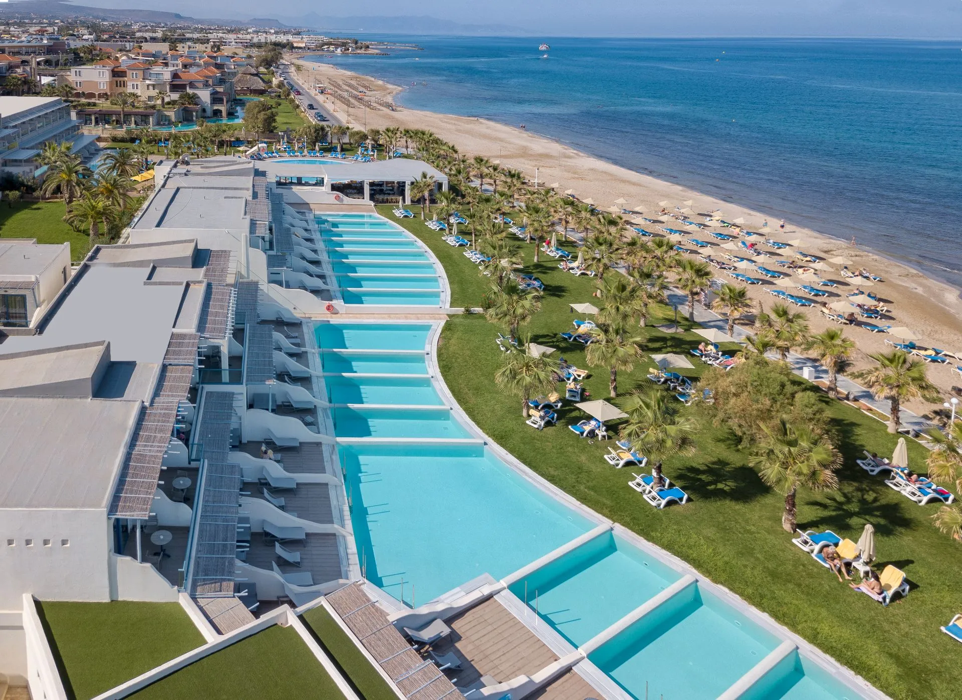 Poolanlage mit Infinity Pool mit weißen Sonnenschirmen und einem jungen Pärchen in einem Mitsis Hotel.