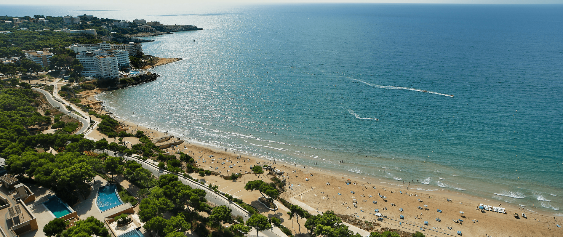 Drohnenaufnahme vom Strand hinauf aufs Meer an einem schönen Sommertag. Der Strand ist gut besucht und auf Meer ziehen Jetskis ihre Bahnen.