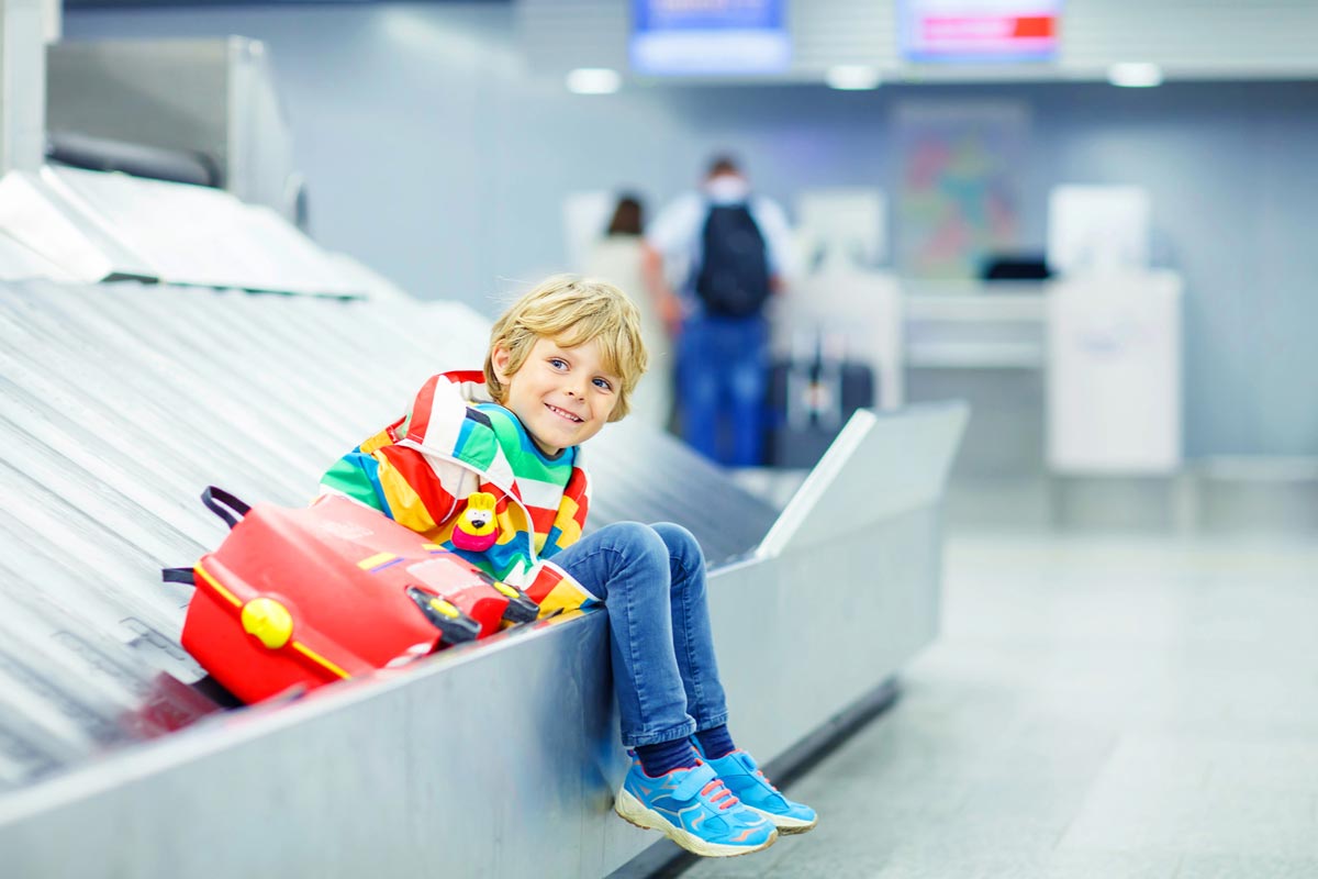 Ein Junge sitzt mit seinem roten Kopfer auf dem Kopferband am Flughafen.