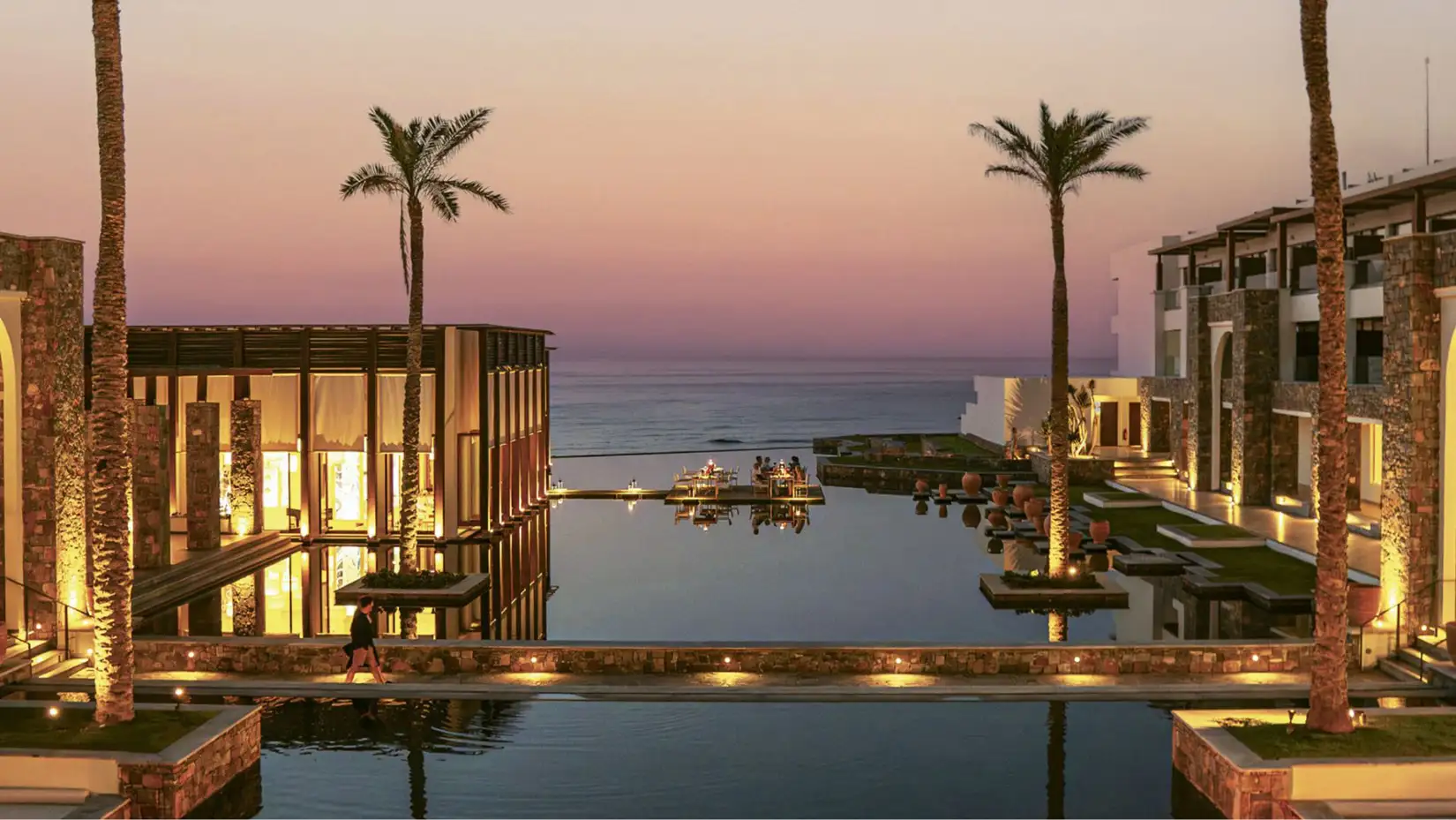 Blick von der Hotelanlage mit Pool und Palmen in der Abenddämmerung auf das Meer.
