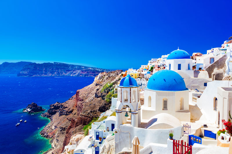 Die berühmte Insel Santorini an einem schönen, strahlenden Sommertag mit wolkenlosem, blauen Himmel. Die Stadt mit ihren charakteristischen weißen Häusern ist auf der rechten Seite des Bildes. Auf der linken Seite ist das Meer und das Festland zu sehen.