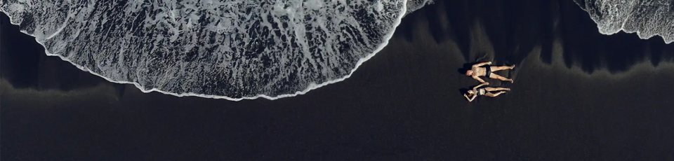 Eltern mit Kind Eltern halten ihre Tochter an den Händen und laufen am Strand aus dem Meerwasser heraus.
