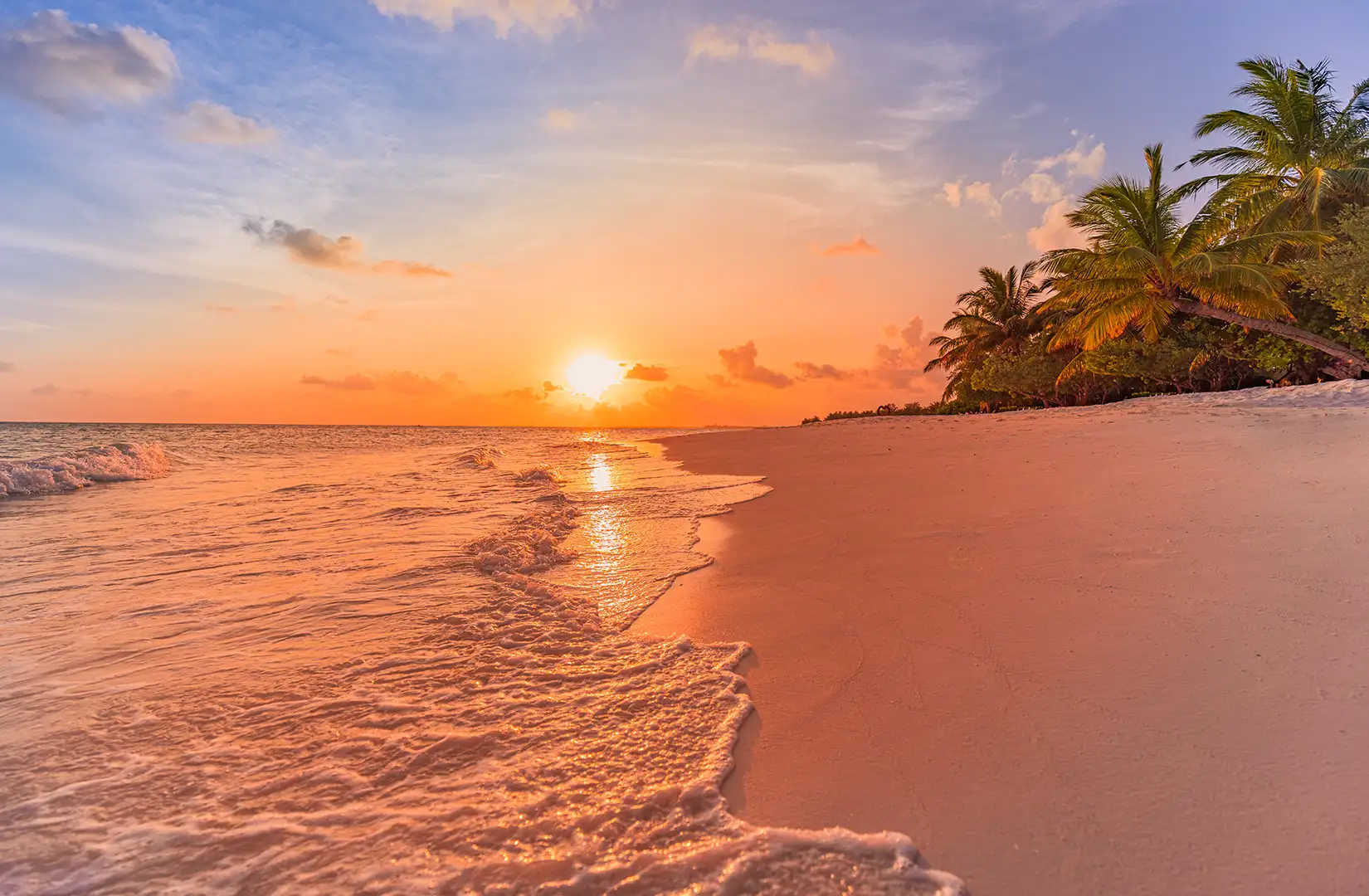 Karibische Inselstrandlandschaft mit ruhigen Meereswellen bei Sonnenuntergang, der die Szenerie in ein weiches orangfarbenedes Licht taucht.