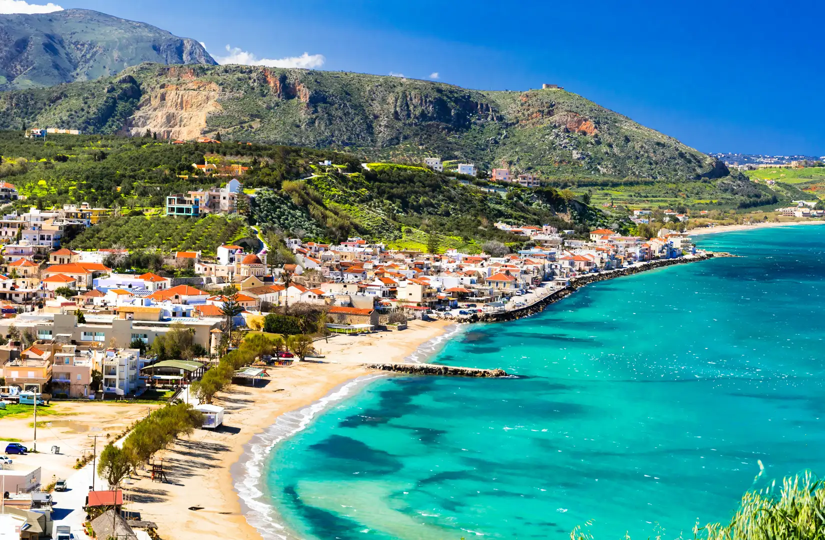 Luftaufnahme herab auf das Dorf Kalyves auf der griechischen Insel Kreta an einem Sommertag. Links das Dorf, an einem Huegel gelegen, rechts die Meeresbucht.
