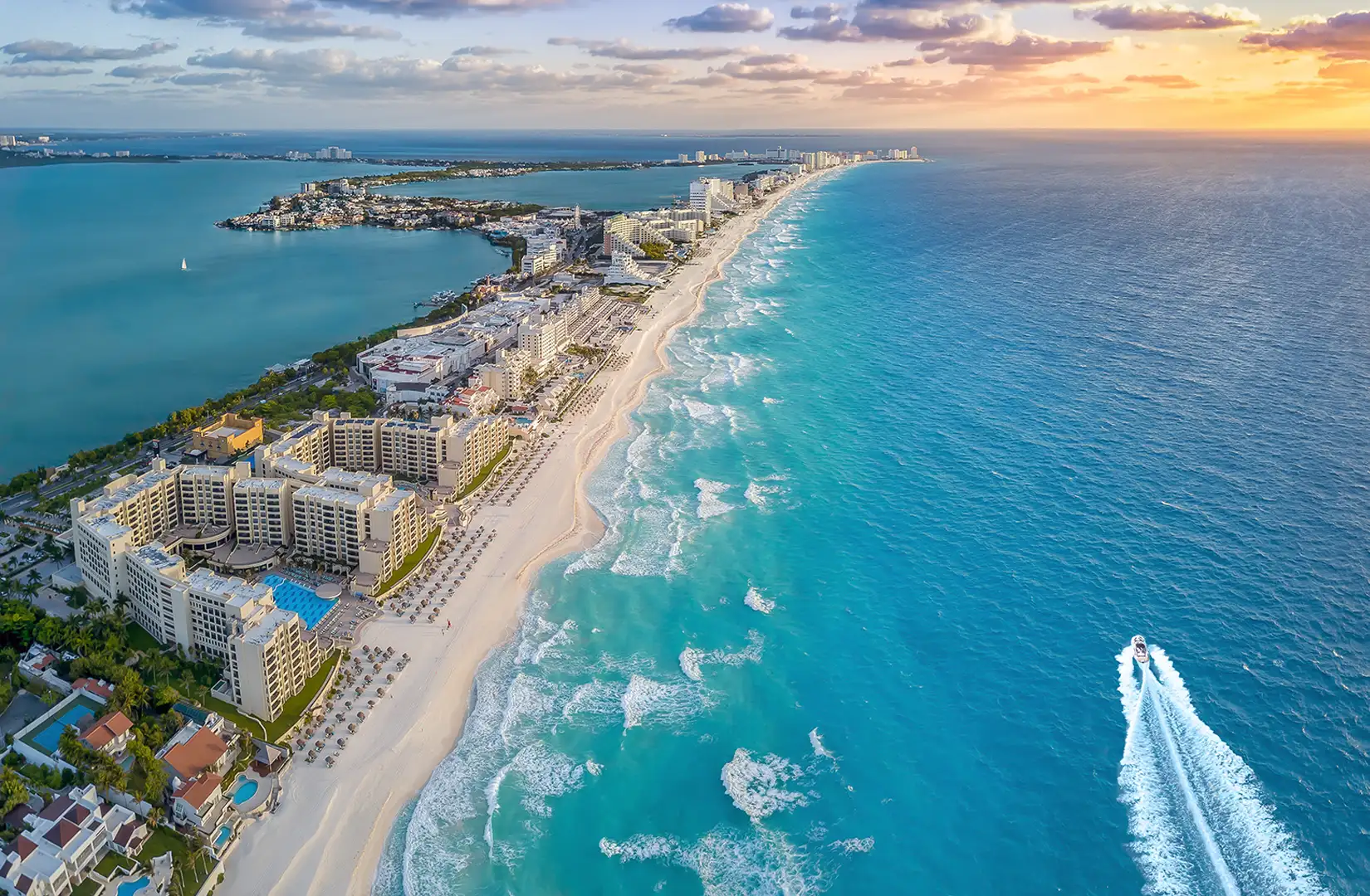 Luftaufnahme vom Strand in Cancun in Mexiko. Der Strand ist mit Hotels bebaut. Im Meer fährt ein Sportboot durch das Bild.