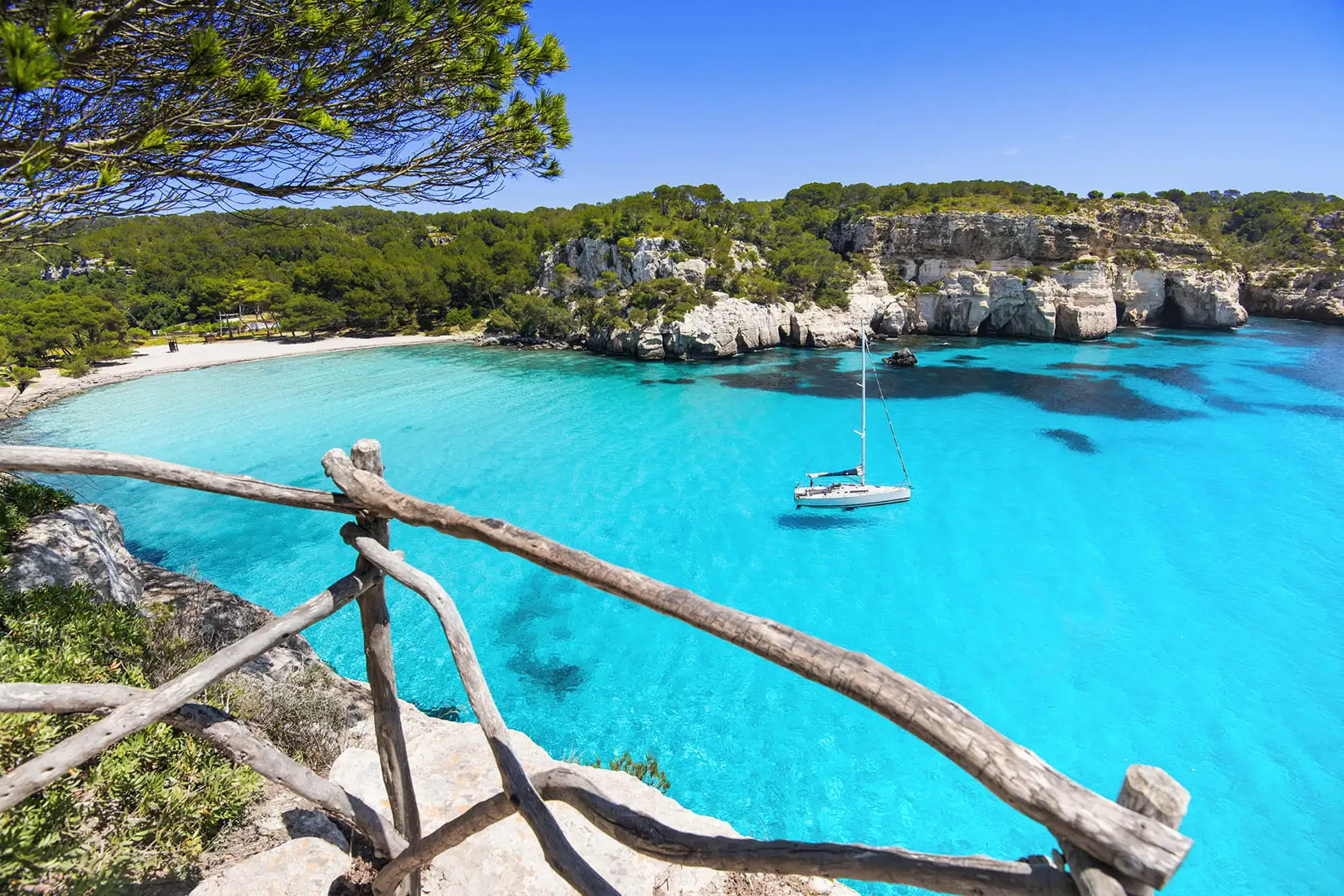 Blick auf Cala en Brut, einen Strand auf Menorca, mit türkisfarbenden Wasser. In der Bucht liegt ein Boot vor Anker.
