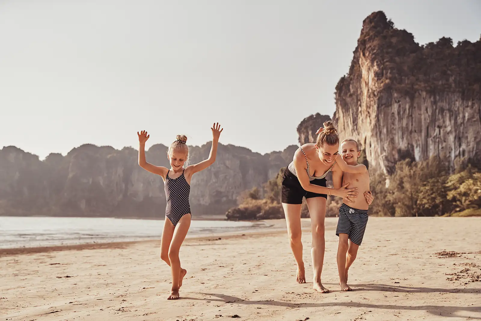  Mutter und mit zwei kleinen Kinder gehen zusammen am Strand spazieren und haben eine gute Zeit im Urlaub.