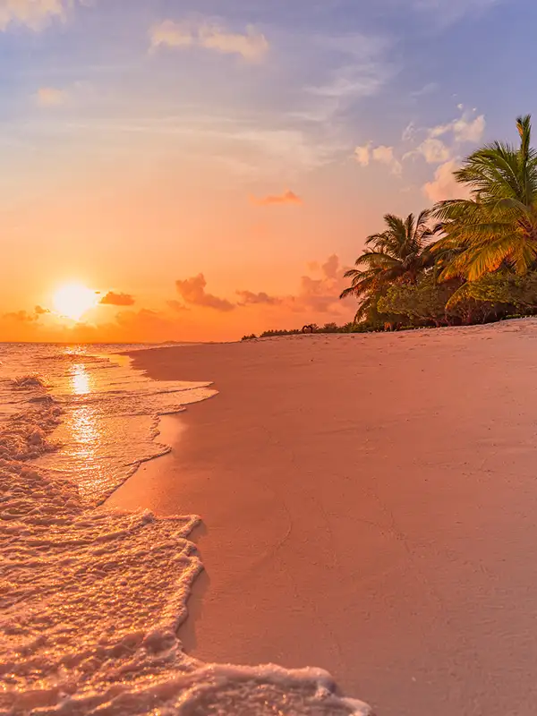 Karibische Inselstrandlandschaft mit ruhigen Meereswellen bei Sonnenuntergang, der die Szenerie in ein weiches orangfarbenedes Licht taucht.