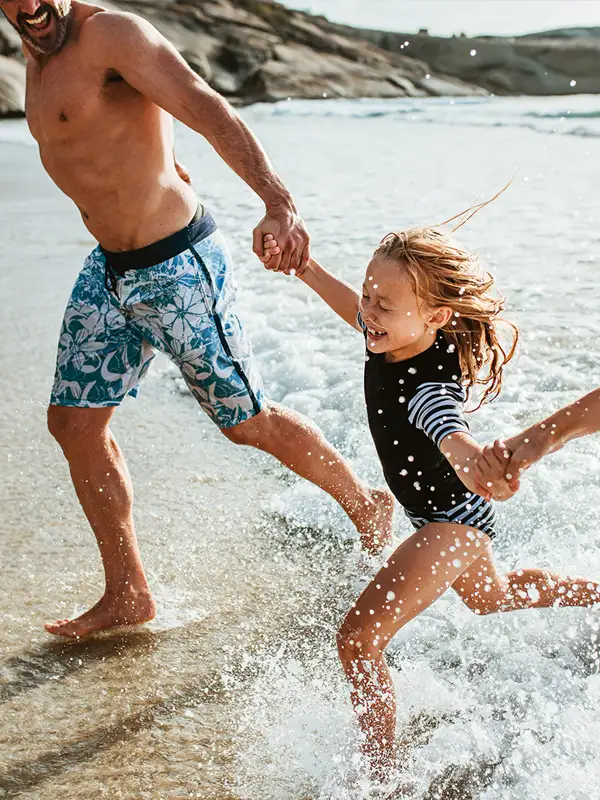 Eltern halten ihre Tochter an den Händen und laufen am Strand aus dem Meerwasser heraus. 