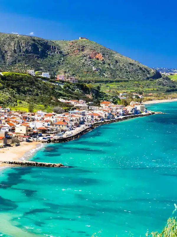 Luftaufnahme herab auf das Dorf Kalyves auf der griechischen Insel Kreta an einem Sommertag. Links das Dorf, an einem Huegel gelegen, rechts die Meeresbucht.