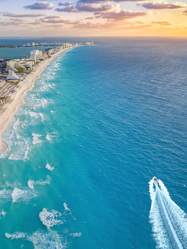 Luftaufnahme vom Strand in Cancun in Mexiko. Der Strand ist mit Hotels bebaut. Im Meer fährt ein Sportboot durch das Bild.