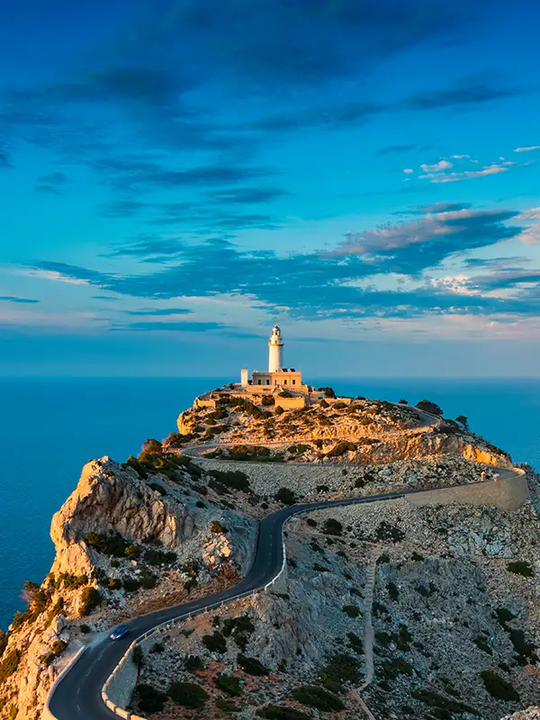 Der berühmte Leuchtturm am Cap de Formentor auf Mallorca bei Abenddämmerung, der einsam auf einem Hügel steht und per Straße angebunden ist.