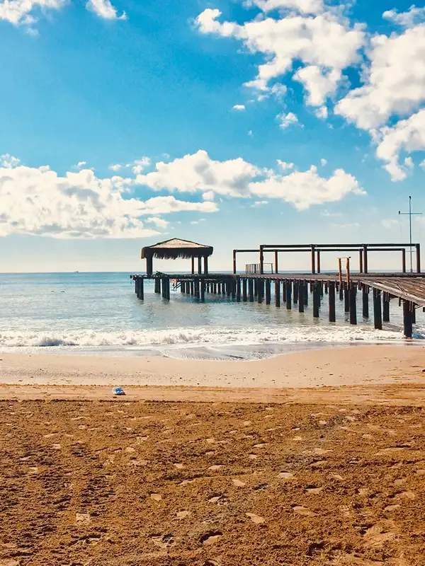 Strand in Belek mit Blick auf das Meer mit Pier bei blauem Himmel an einem Sommertag..