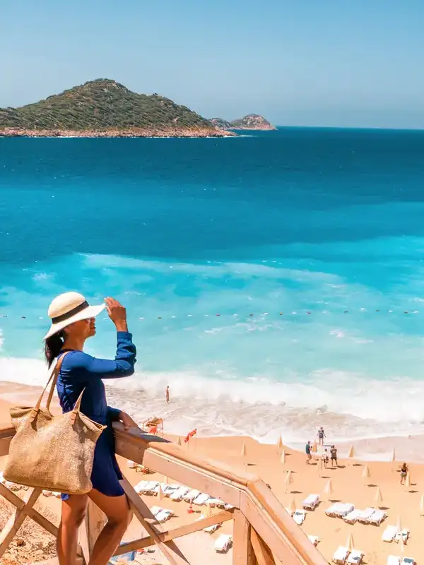 Junge Frau mit Hut im blauen Kleid auf einer Anhöhe blickt an einem schönen Sommertag auf den Strand von Kaputas herab.
