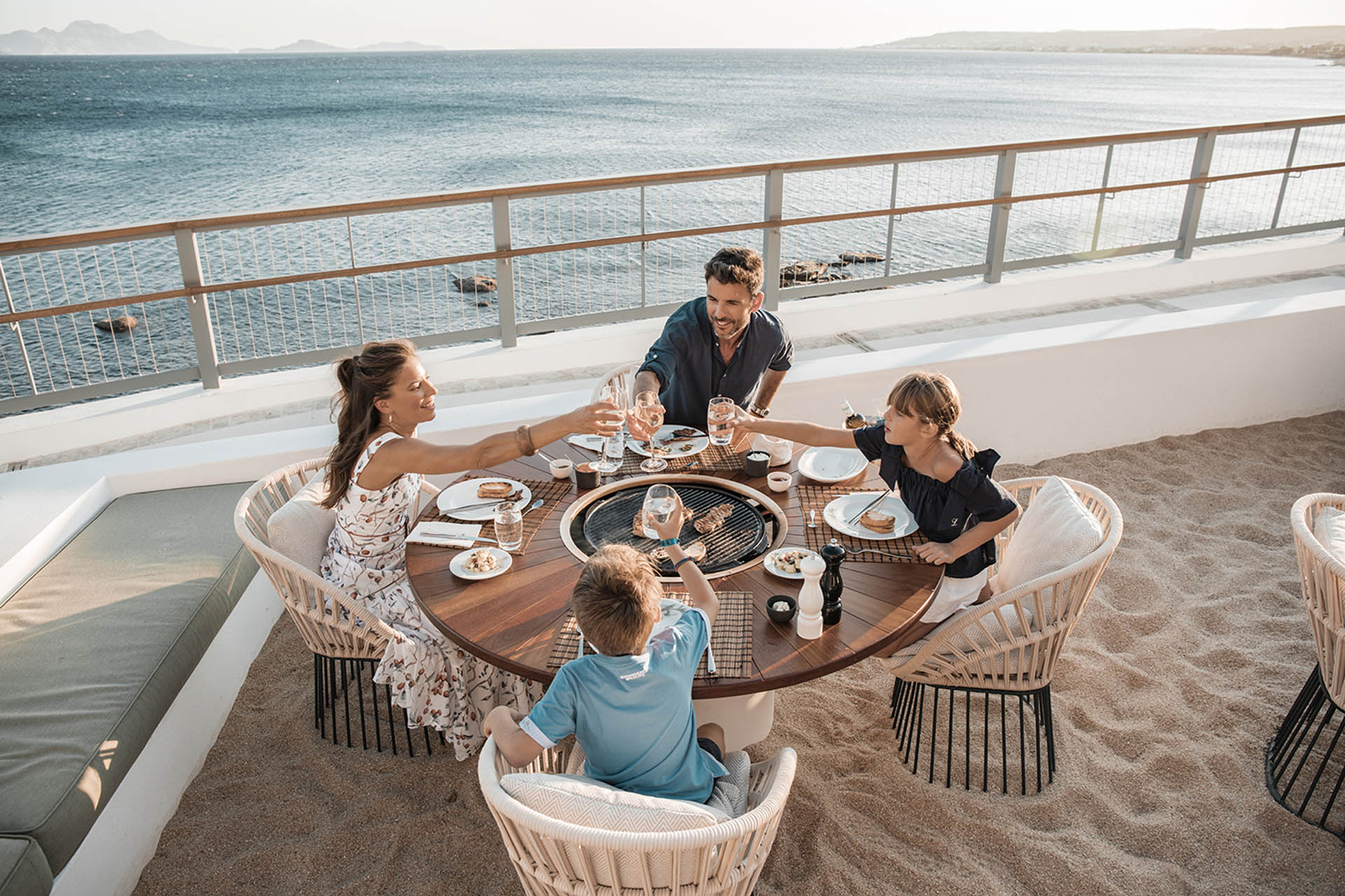Familie mit zwei Kindern beim Essen. Alle stoßen gerade mit den Gläsern an.