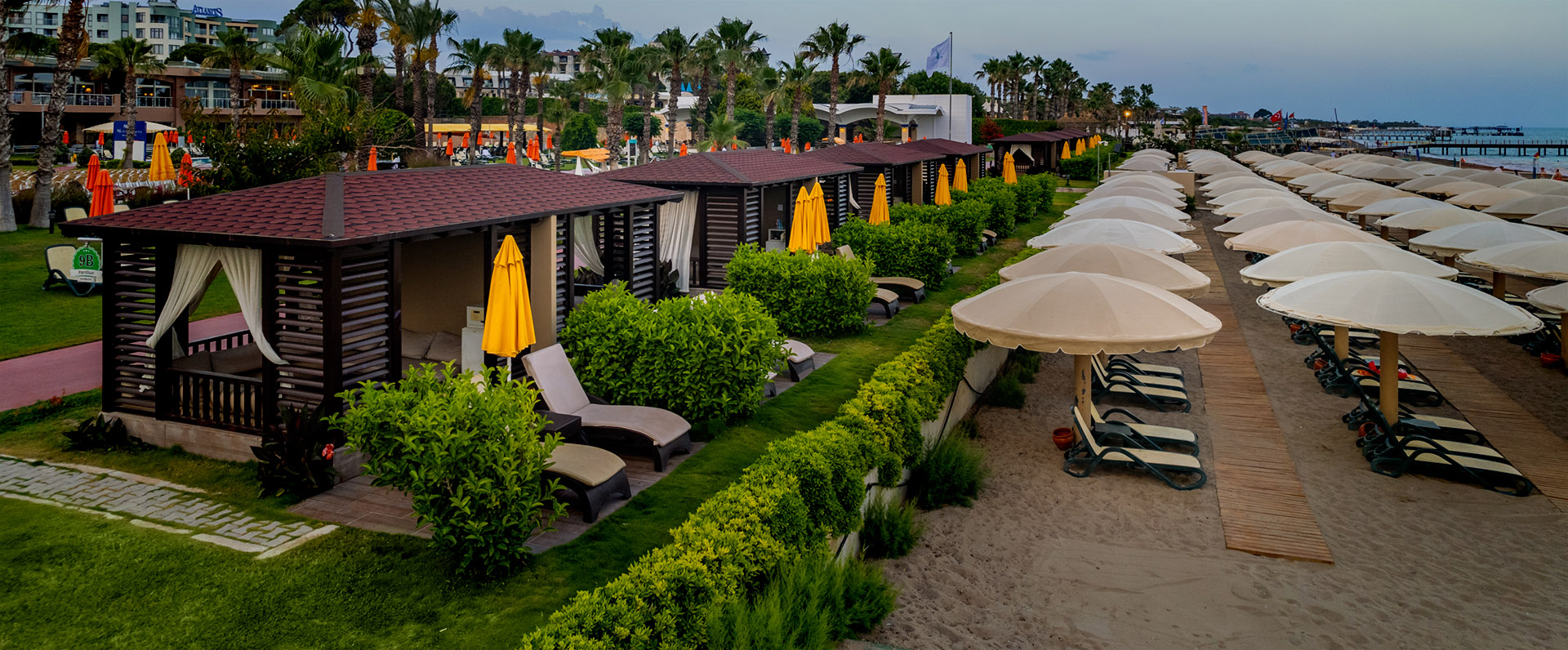 Hotelanlage des Pine Beach am Strand mit Sonnenliegen. 